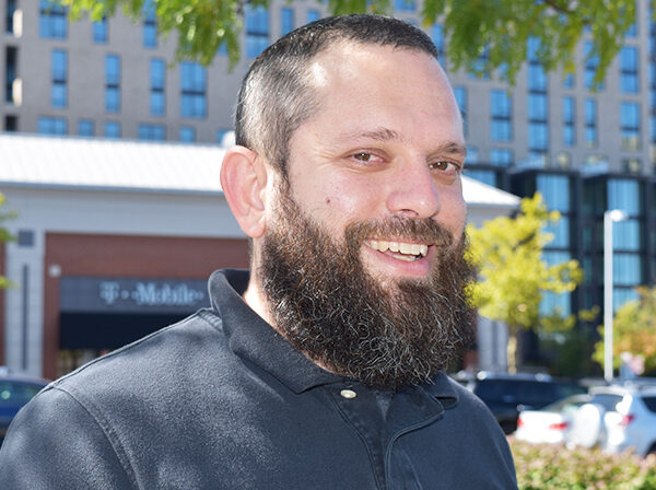 Matt Starr, NV Rides volunteer standing with a building and green trees in the backdrop. He's happy because transportation for seniors is now solved!