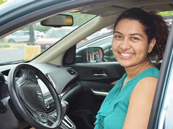 Smiling NV Rides volunteer, Rhea Sharma. She is sitting in the driver seat of a car. She's happy because transportation for seniors is now solved!